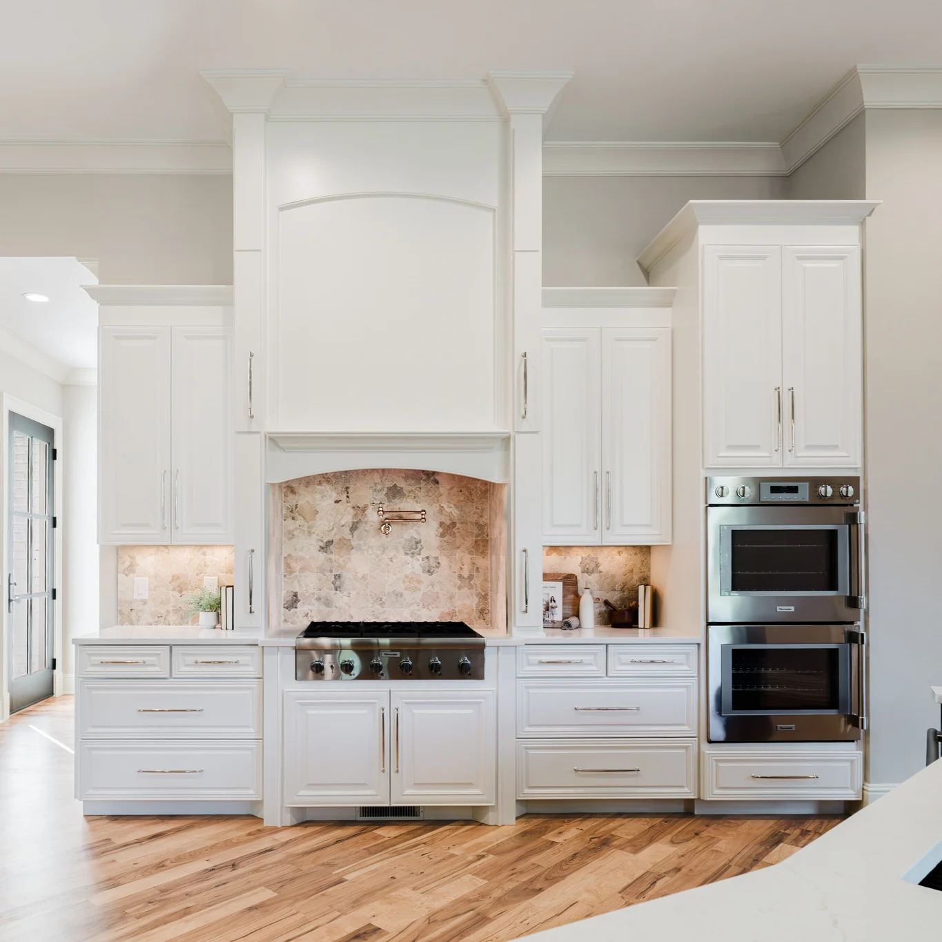 Finished Oxmoor kitchen range wall with white cabinetry, a custom hood, stone backsplash, and double ovens