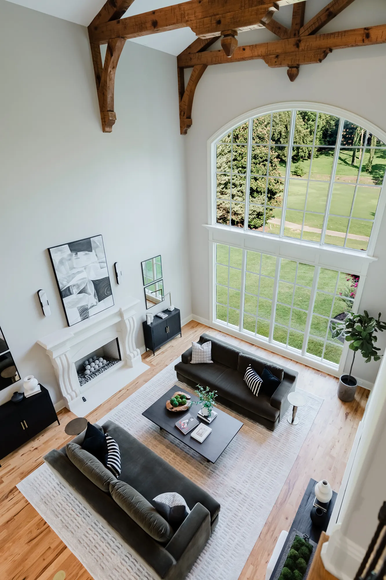 Two-story great room with exposed timber trusses and a tall arched window, seen from the mezzanine