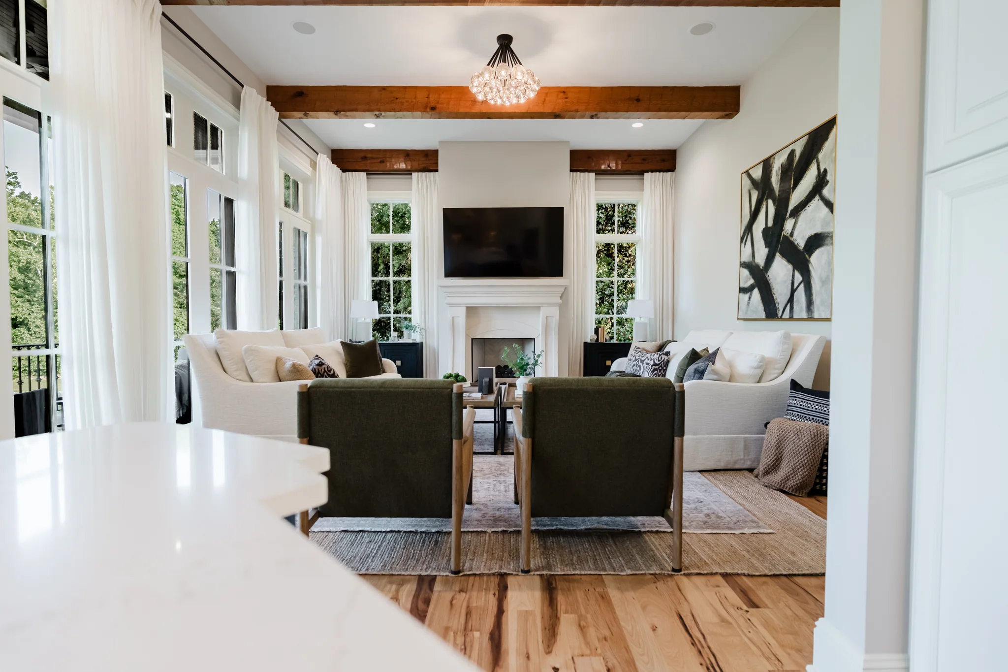 Wide view of the keeping room with exposed beams, a cast-stone fireplace, and windows down both walls