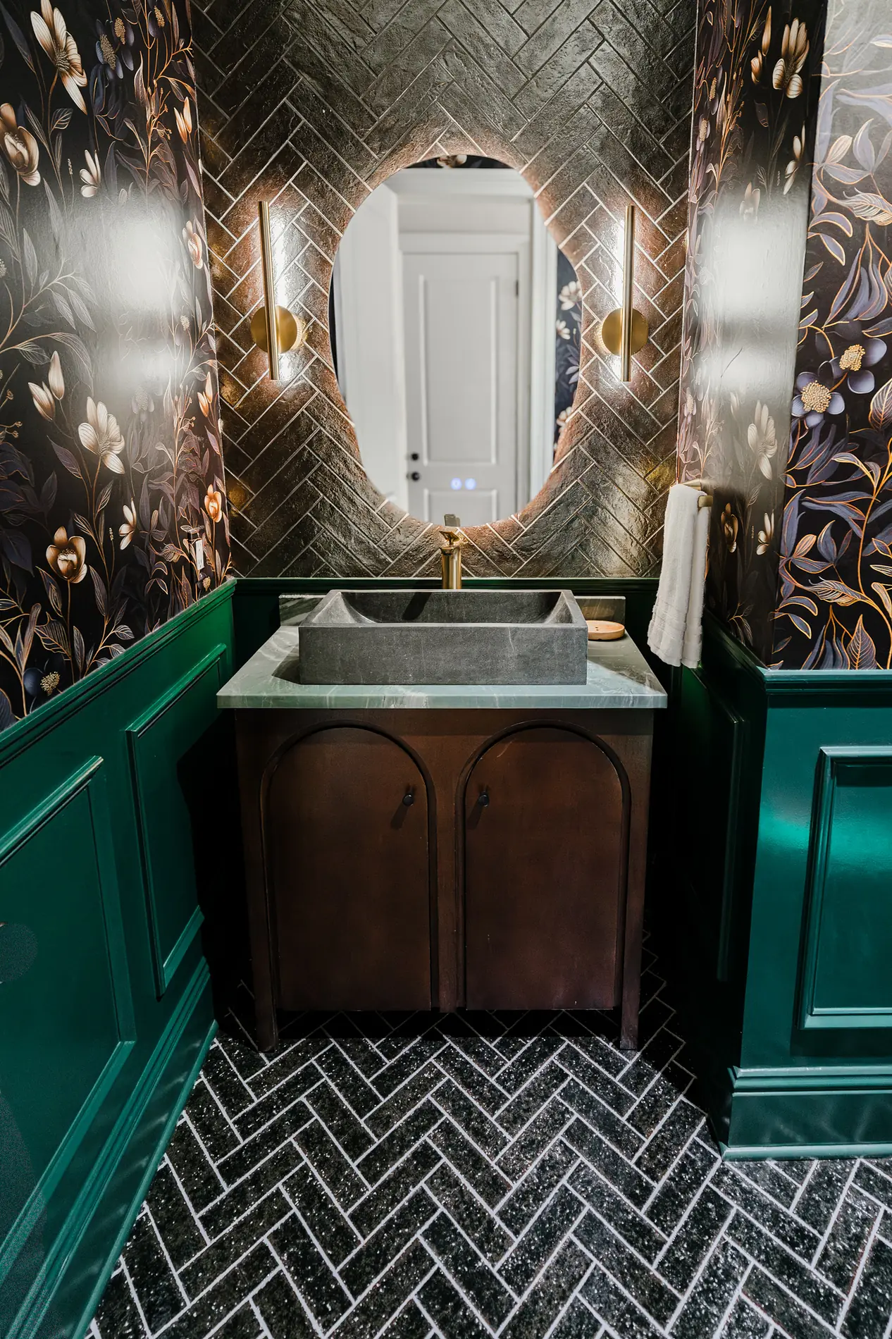 Powder room with emerald panelled millwork, floral wallpaper, and a black herringbone tile floor