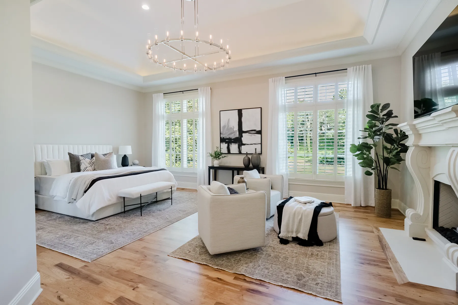 Primary bedroom with a tray ceiling, ring chandelier, and a bay window of plantation shutters