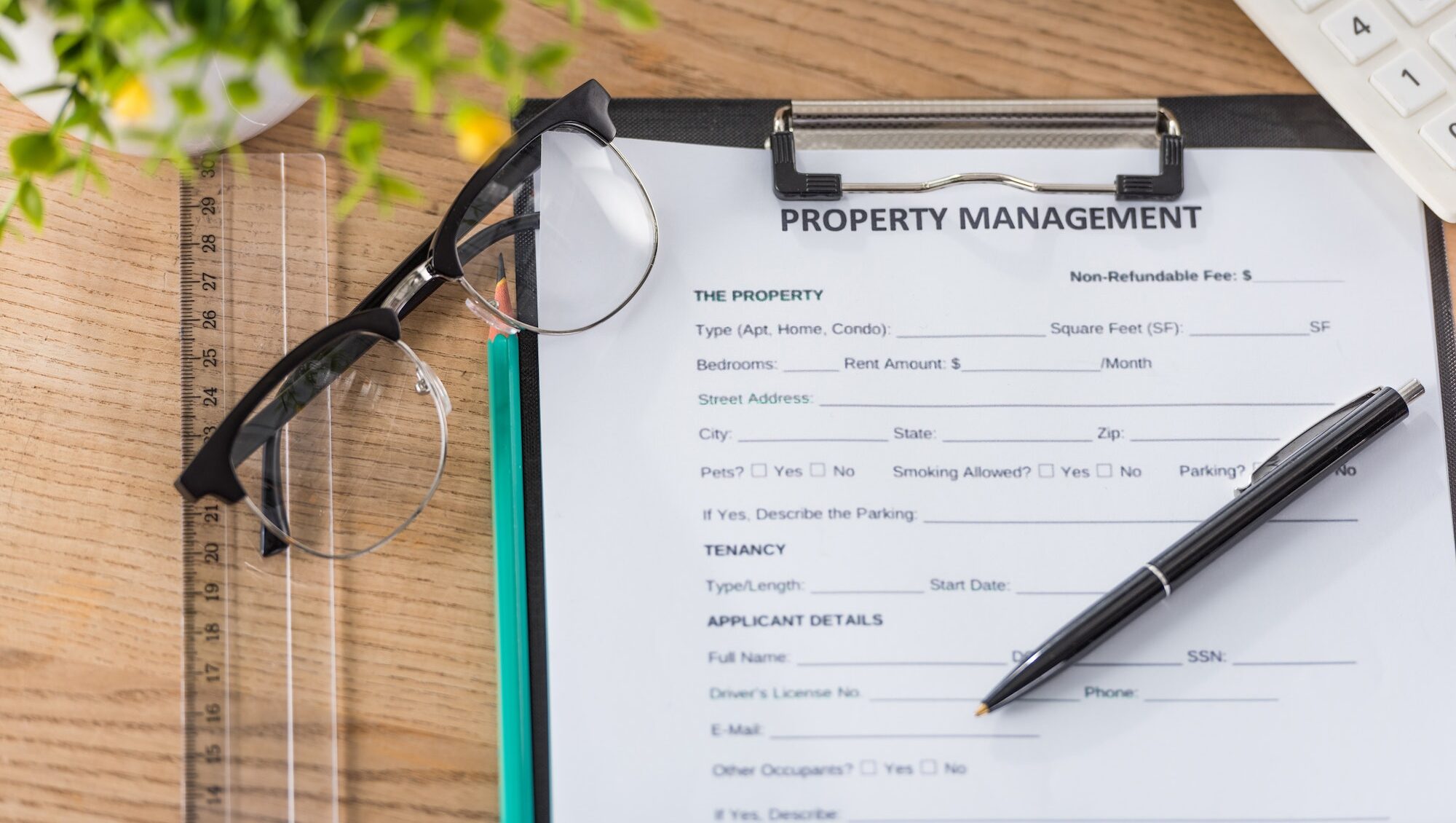 top view of clipboard with property management agreement, pen, glasses, calculator and green plant